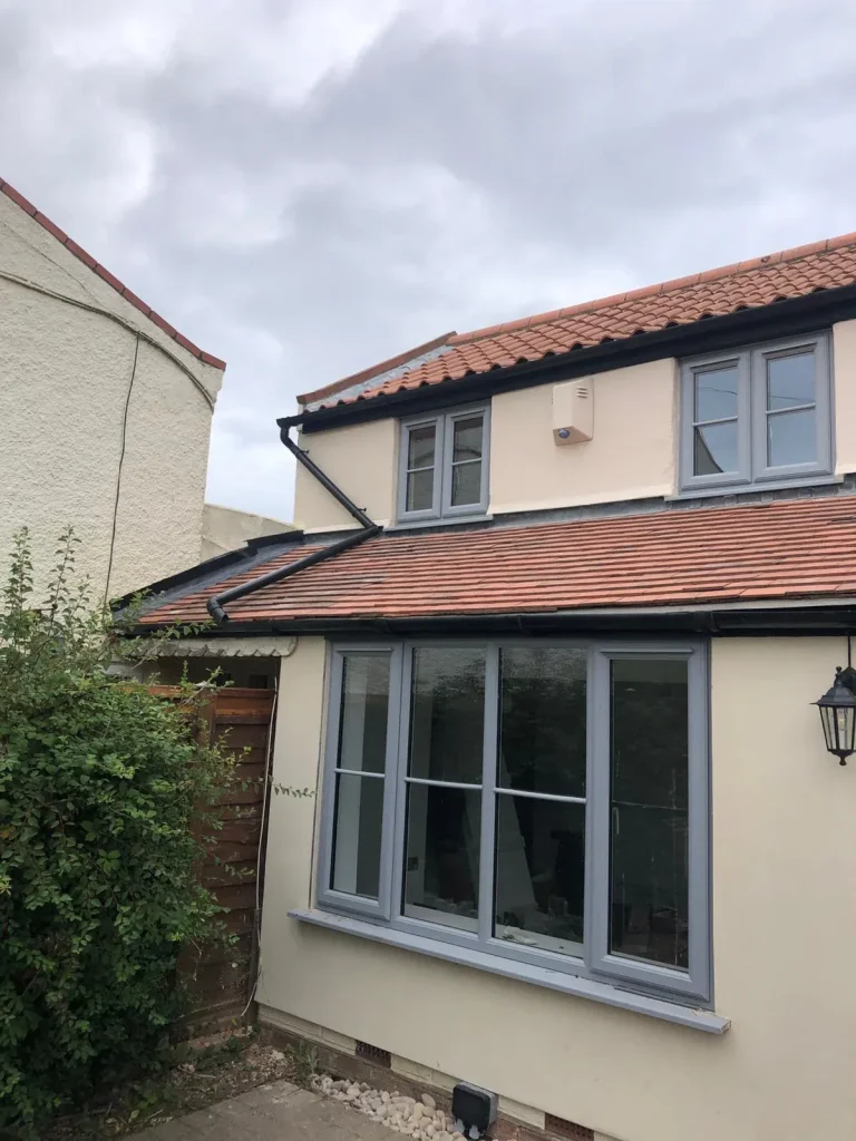 Decorated house exterior with cream render, grey window frames and a tiled roof