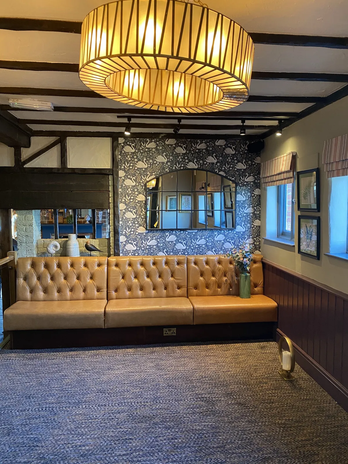 Seating area with geometric wallpaper behind a leather banquette and navy panelling
